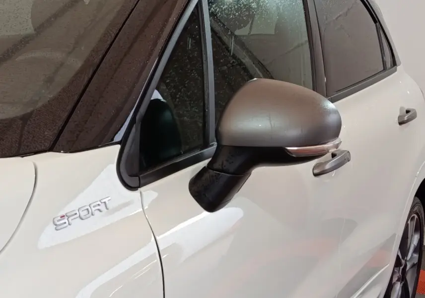 Gros plan sur le rétroviseur côté gauche et l’inscription Sport d’une FIAT 500X blanche avec toit noir.