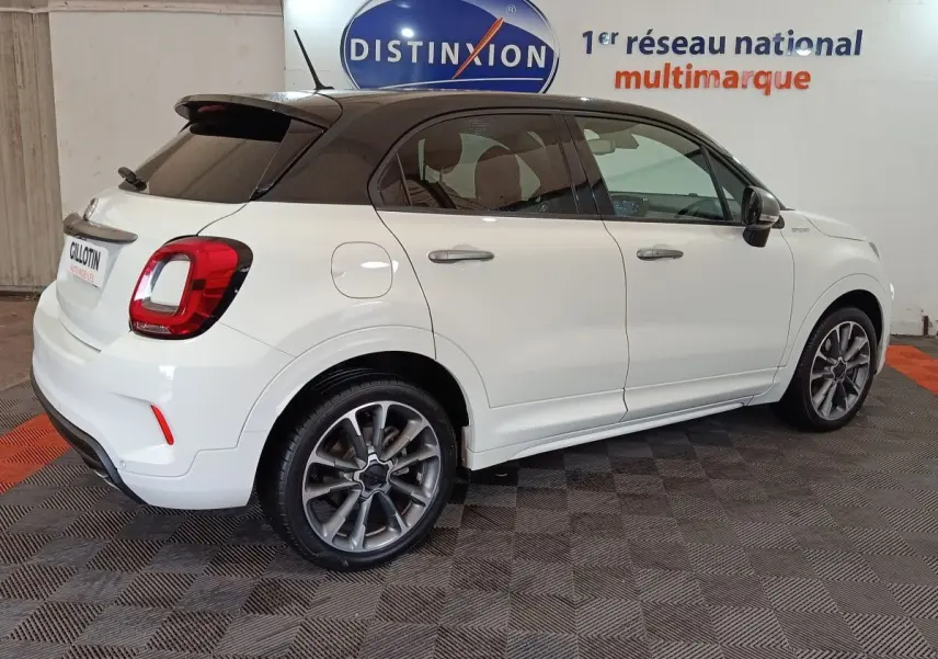 Vue 3/4 arrière droite d'une FIAT 500X blanche avec toit noir, feux arrière LED et jantes alliage sport.