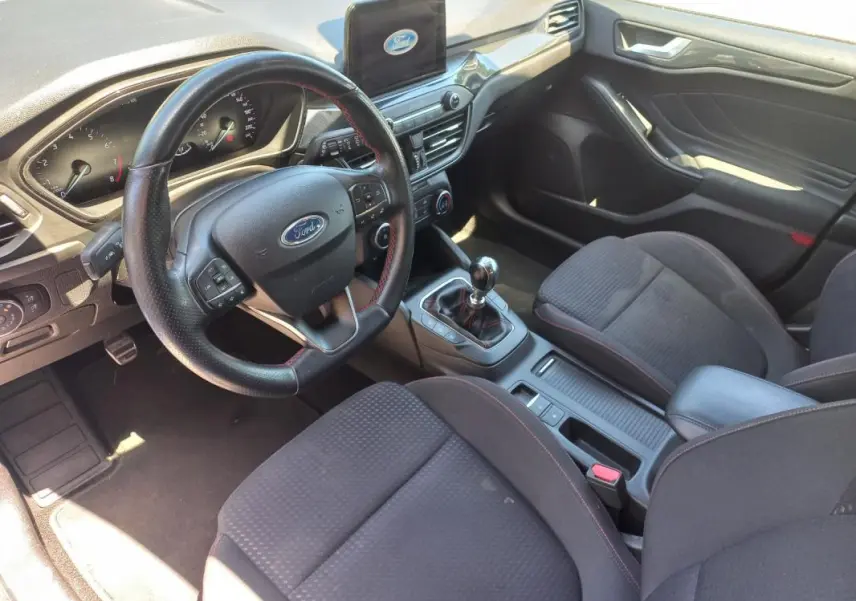 Vue intérieure côté conducteur de la Ford Focus 2019 avec volant cuir, écran central et levier de vitesse manuel.