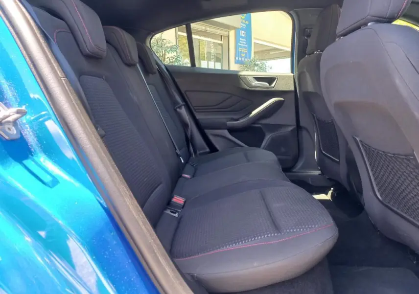 Vue intérieure arrière gauche de la Ford Focus ST-Line bleu 2019, sièges noirs avec surpiqûres rouges et portes ouvertes.