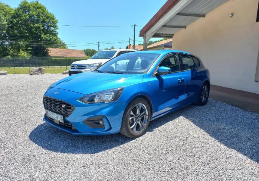 Ford Focus 1.0 SCTI ST-LINE bleu vue 3/4 avant droit, avec calandre noire et jantes alliage distinctives.