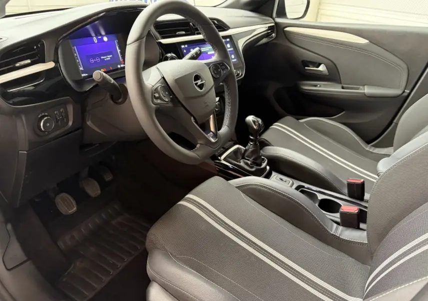 Vue intérieure côté conducteur de l’Opel Corsa 2025, volant multifonctions cuir synthétique et sièges tissu gris à bandes claires.