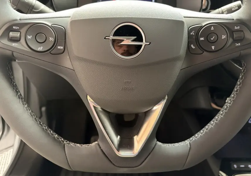 Gros plan sur le volant cuir synthétique noir de l'Opel Corsa 2025 avec commandes multifonctions et logo central chromé.