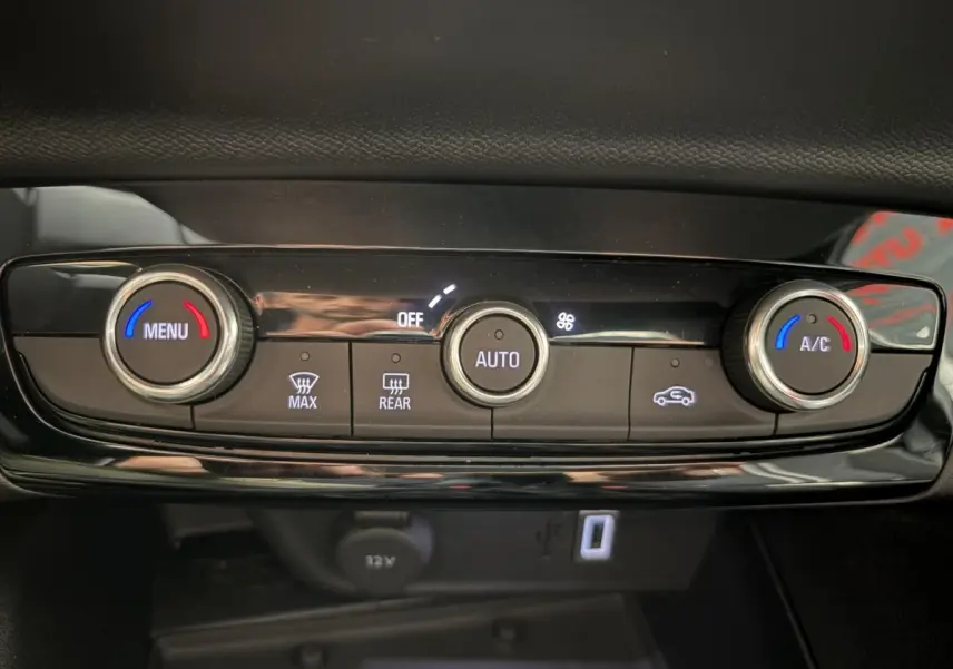 Gros plan sur la console centrale noire de l’Opel Corsa 2025, montrant les commandes de climatisation et prise 12V.