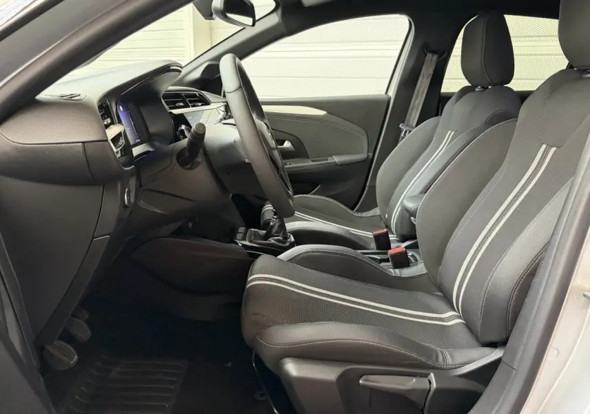 Vue intérieure côté conducteur de l'Opel Corsa 2025 gris clair, sièges noirs avec bandes blanches et volant multifonctions.