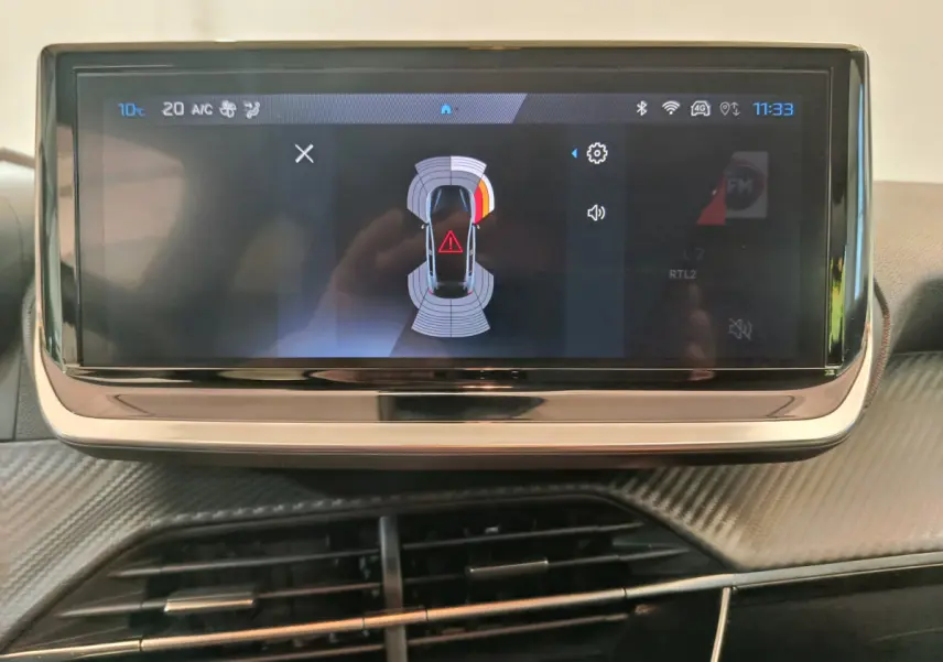 Écran tactile central affichant l'aide au stationnement avec vue aérienne du Peugeot 208 gris foncé, intérieur moderne.