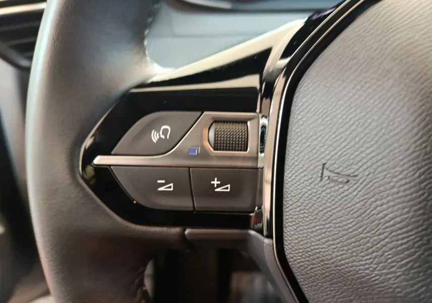 Gros plan sur les commandes vocales et volume au volant cuir noir de la Peugeot 208 PureTech 100 S&S Allure 2025.