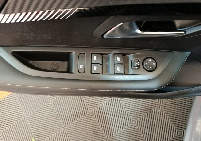 Vue rapprochée des commandes de lève-vitres et rétroviseurs sur la porte côté conducteur d'une Peugeot 208 gris foncé.