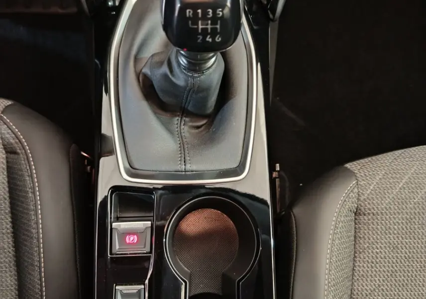 Vue plongeante sur la console centrale noire de la Peugeot 208 PureTech 100, avec levier de vitesses manuel et porte-gobelets.