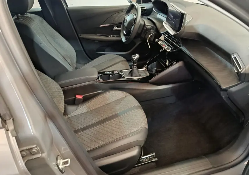 Vue intérieure côté conducteur de la Peugeot 208 PureTech 100 S&S Allure 2025 avec sellerie grise et tableau de bord moderne.