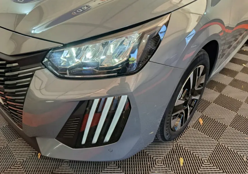 Gros plan sur l'avant droit gris foncé du Peugeot 208 2025, mettant en valeur les phares LED et la calandre distinctive.