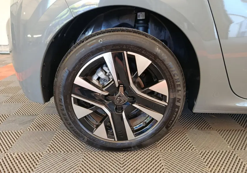 Gros plan sur la roue avant gauche de la Peugeot 208 gris foncé avec jante alliage bicolore et logo Peugeot central.