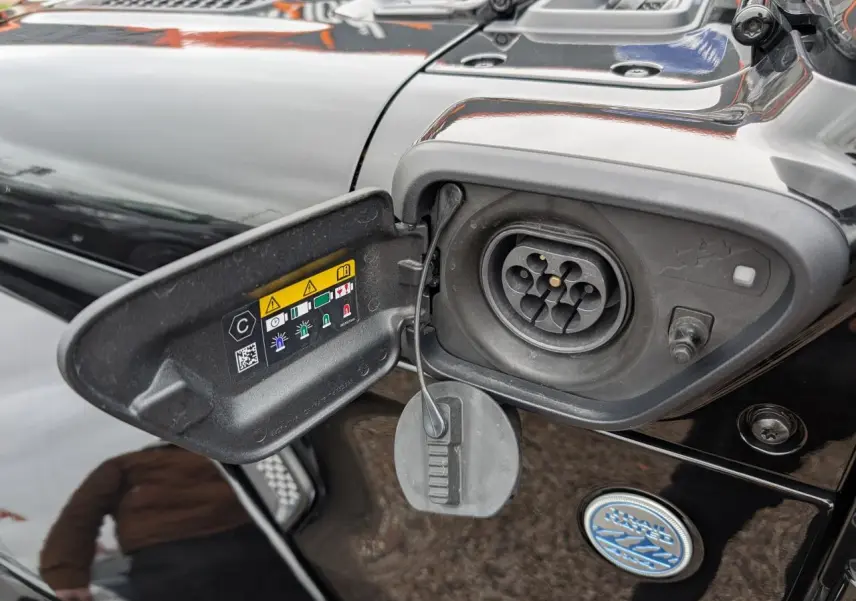 Détail de la prise de recharge hybride côté gauche d’un Jeep Wrangler noir avec port ouvert et instructions visibles.