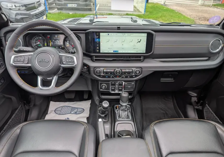 Vue intérieure avant du Jeep Wrangler 2024 noir, tableau de bord moderne avec écran tactile large et volant multifonctions.