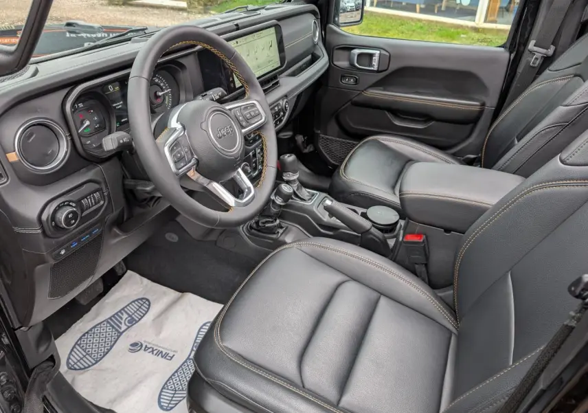 Vue intérieure côté conducteur de la Jeep Wrangler 2024, sellerie cuir noire avec surpiqûres jaunes et tableau de bord numérique.