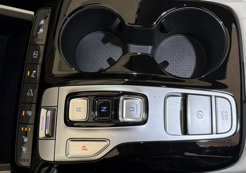 Vue rapprochée de la console centrale noire et argentée du Hyundai Tucson 1.6 Hybrid 230 Executive avec commandes de boîte auto et porte-gobelets.