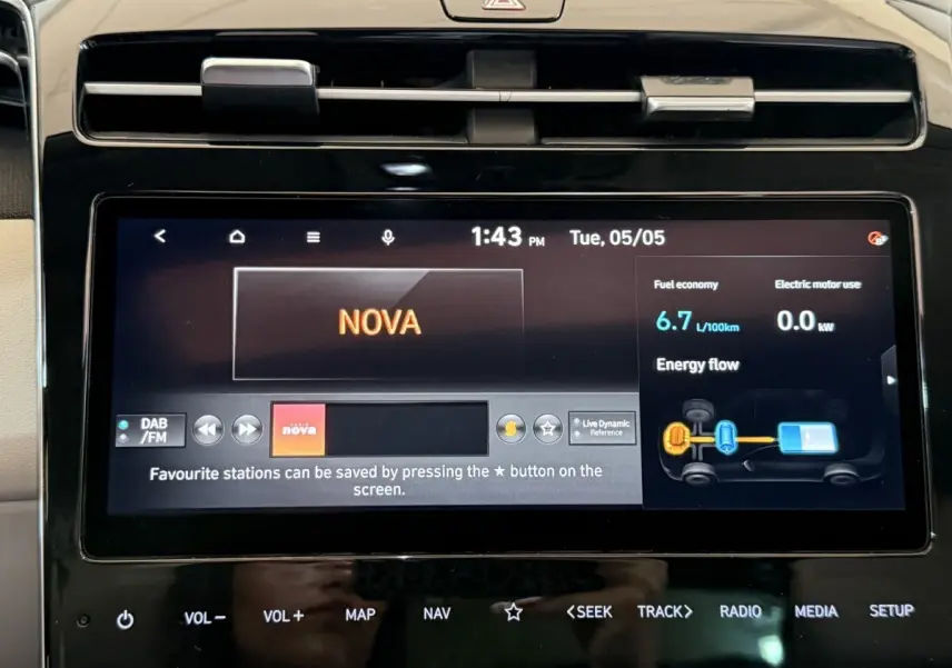 Écran tactile central du Hyundai Tucson gris foncé, affichant radio et consommation hybride, vue intérieure frontale.