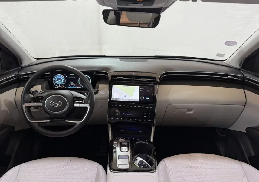 Vue intérieure avant du Hyundai Tucson 1.6 Hybrid 230 Executive avec tableau de bord beige et écran tactile central.