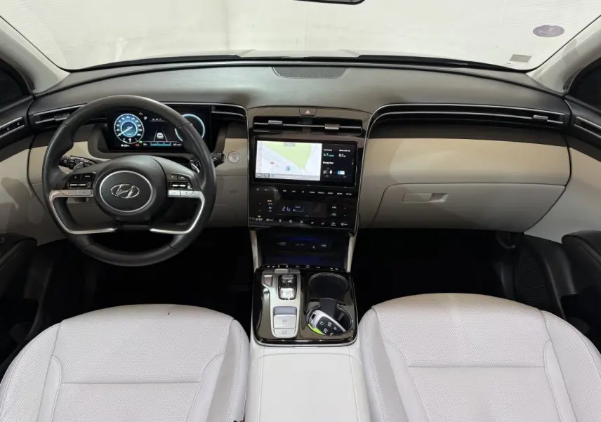 Vue intérieure frontale du Hyundai Tucson 1.6 Hybrid 230 Executive, avec tableau de bord noir et sièges cuir blanc.