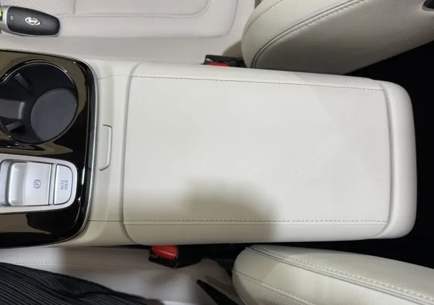 Vue rapprochée de la console centrale beige clair du Hyundai Tucson 1.6 Hybrid 230 Executive avec commandes de frein et porte-gobelet.