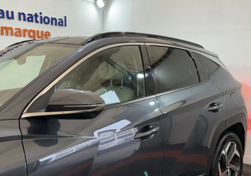 Vue de profil côté gauche du Hyundai Tucson gris foncé 1.6 Hybrid 230 Executive avec jantes alliage et barres de toit.