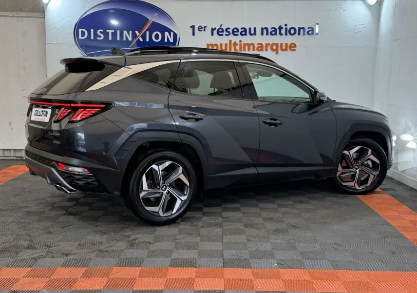 Vue latérale droite d'un Hyundai Tucson 1.6 Hybrid gris foncé avec jantes alliage et toit noir, en intérieur showroom.
