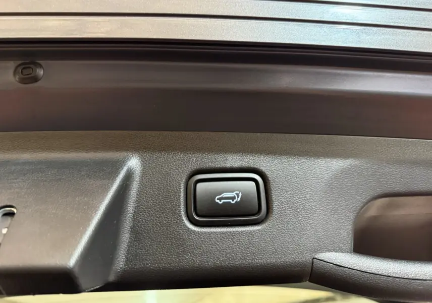 Gros plan sur le bouton d'ouverture électrique du coffre du Hyundai Tucson gris foncé, intérieur du hayon visible.