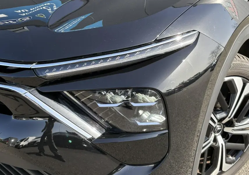 Gros plan sur le phare avant droit et la jante alliage noire diamantée du Citroën C5 X Noir Perla 2024.
