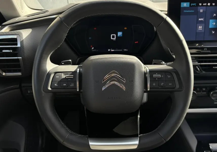 Vue rapprochée du volant cuir noir du Citroën C5 X 2024 avec commandes intégrées et tableau de bord numérique.