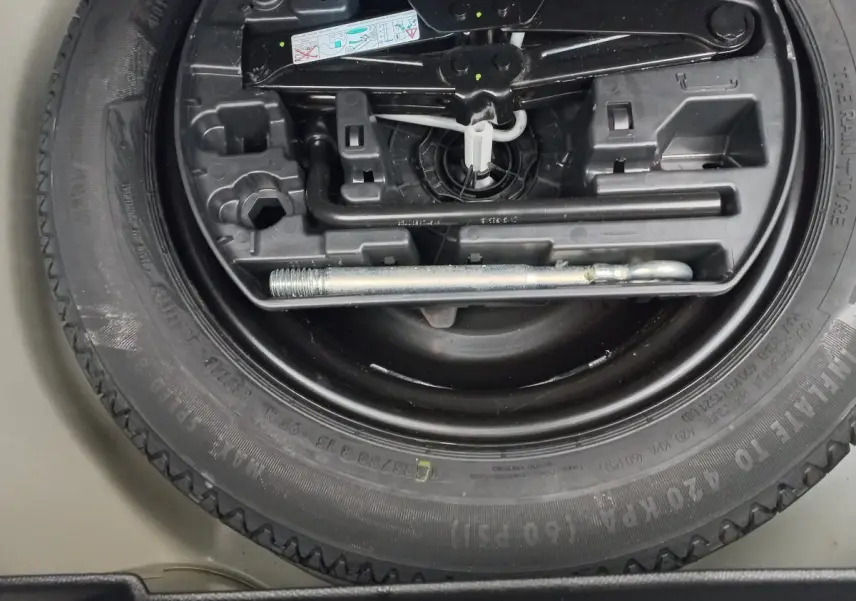 Gros plan sur la roue de secours noire et les outils de bord du coffre d’une Peugeot 208 blanche.