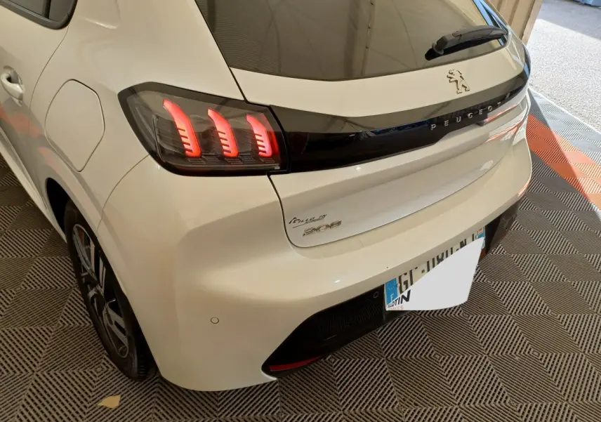 Vue 3/4 arrière droite d'une Peugeot 208 blanche avec feux arrière LED et logo Peugeot sur la malle.