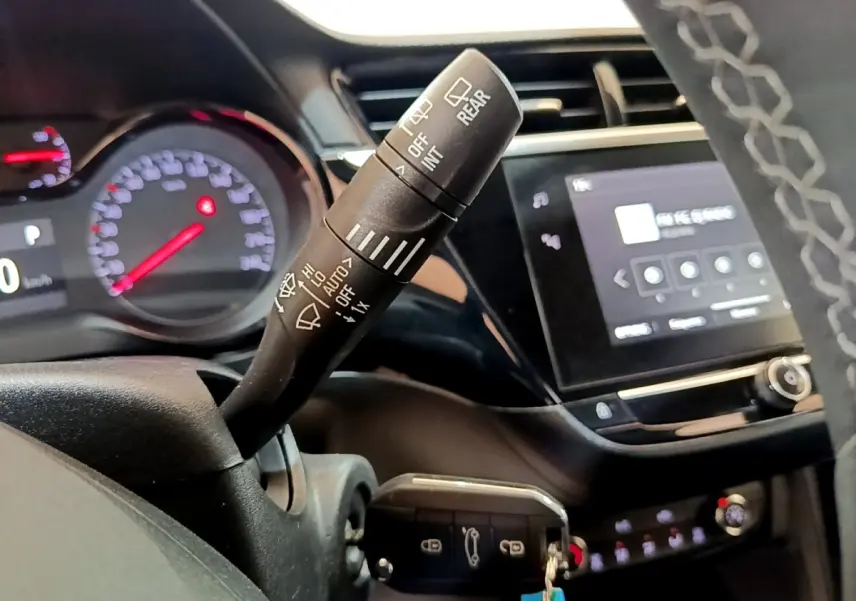 Gros plan sur la commande d’essuie-glace à gauche du volant dans l’habitacle noir de l’Opel Corsa blanche 2023.