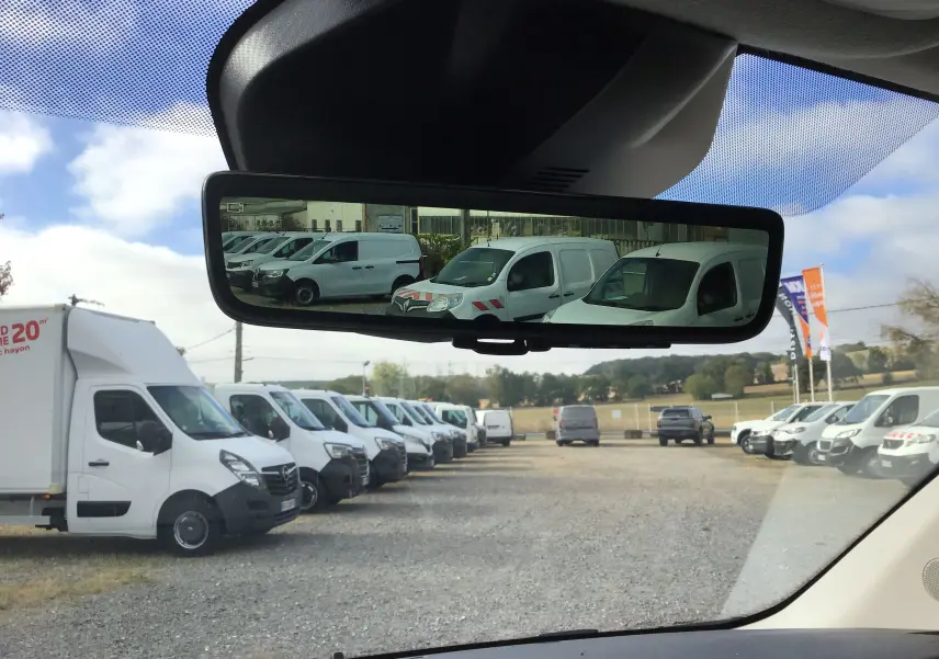 Vue depuis l'intérieur vers l'arrière, reflet dans le rétroviseur d'une rangée de véhicules utilitaires blancs, PEUGEOT Expert noir non visible.