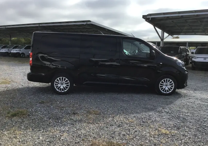 Vue de profil côté gauche d’un Peugeot Expert cabine approfondie noir stationné sur un sol gravillonné.