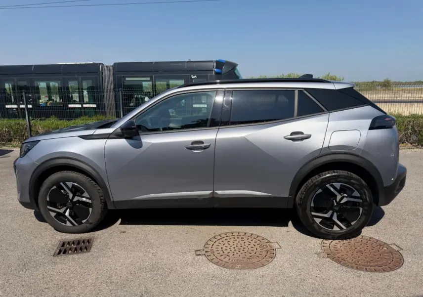 Vue latérale droite d’un Peugeot 2008 Hybrid 145 gris 2025, soulignant ses jantes noires et son design moderne.