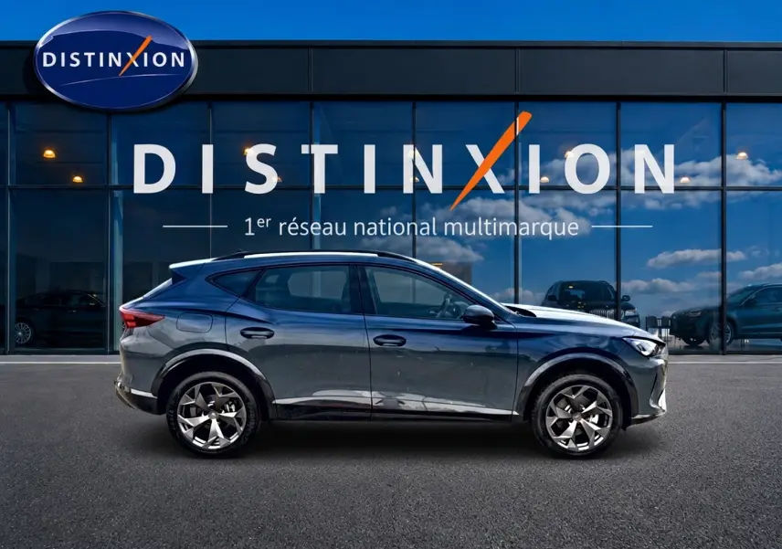 Vue de profil côté gauche du CUPRA Formentor 1.5 etsi hybrid 150 DSG7 en bleu fjord devant une vitrine Distinxion.