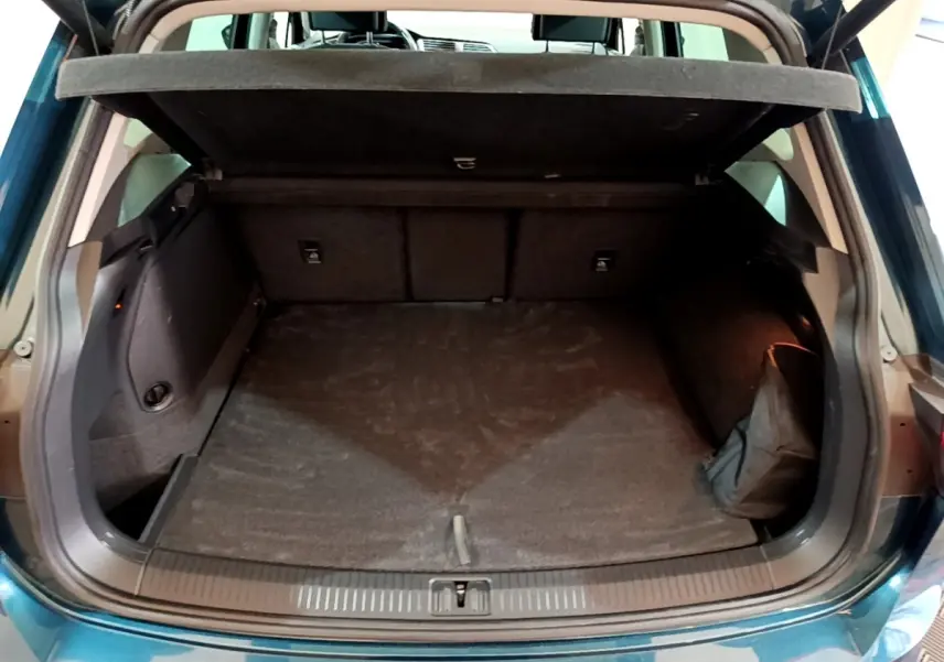 Coffre ouvert vu de l'arrière d'un Volkswagen Tiguan bleu, montrant un espace de rangement vide et la tablette cache-bagages.