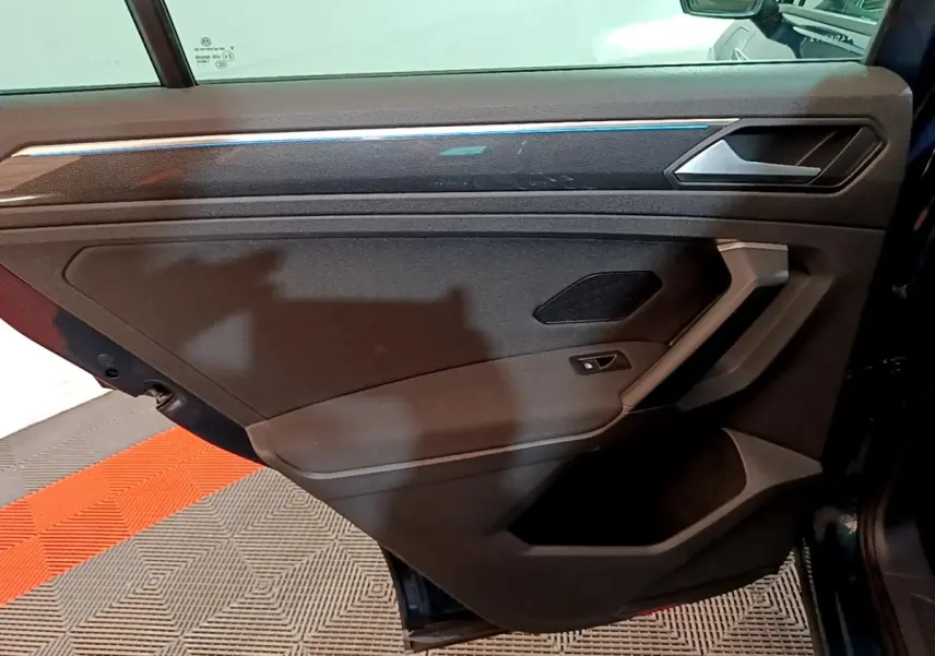 Vue intérieure de la porte arrière droite du Volkswagen Tiguan bleu, avec poignée argentée et haut-parleur intégré.