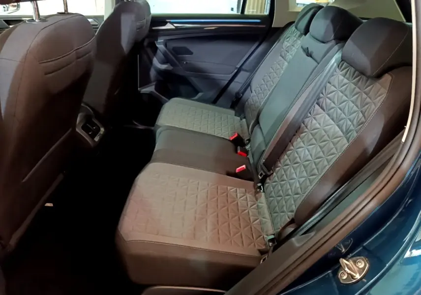 Vue latérale intérieure sur la banquette arrière grise du Volkswagen Tiguan bleu, avec motifs géométriques et ceintures visibles.