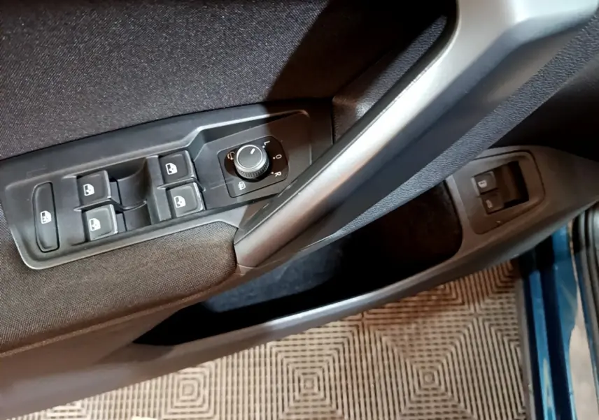 Vue rapprochée du panneau de commandes des vitres et rétroviseurs côté conducteur d’un Volkswagen Tiguan bleu.