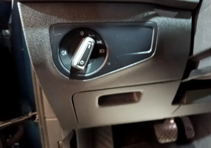 Gros plan sur le bouton de commande des phares noir et argenté, intérieur côté conducteur du Volkswagen Tiguan bleu hybride.