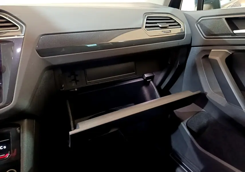 Vue intérieure côté passager du Volkswagen Tiguan bleu 2021, boîte à gants ouverte et tableau de bord noir.