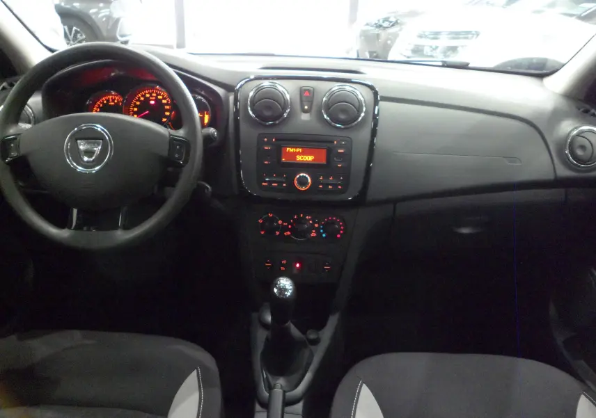 Vue intérieure frontale du tableau de bord et volant d'une Dacia Sandero Stepway 2016 avec commandes manuelles et affichage radio orange.