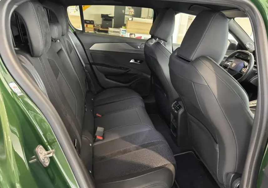 Vue intérieure arrière côté gauche d’une Peugeot 308 GT 2024 vert, montrant la banquette et les sièges avant en sellerie tri matières noire.
