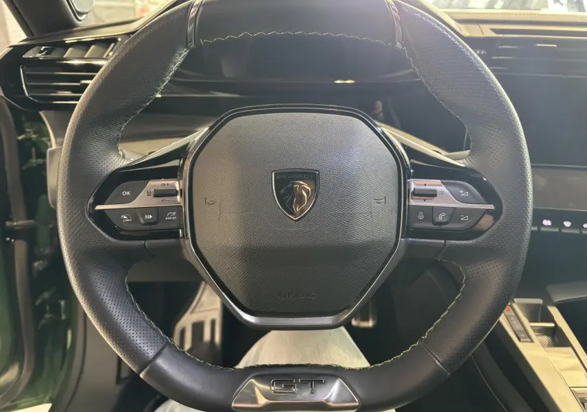 Vue rapprochée du volant cuir noir avec surpiqûres vertes et logo GT de la Peugeot 308 2024 vert.