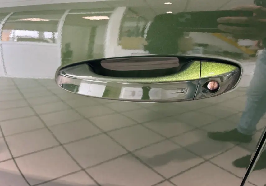 Poignée de porte côté gauche vert métallisé sur Peugeot 308 2024, reflet intérieur et serrure visible.