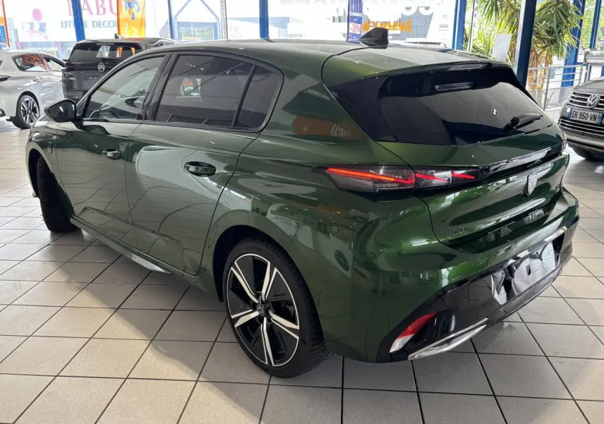 Vue 3/4 arrière gauche d'une Peugeot 308 berline GT 2024 vert métallisé avec jantes alliage et feux arrière LED griffés.