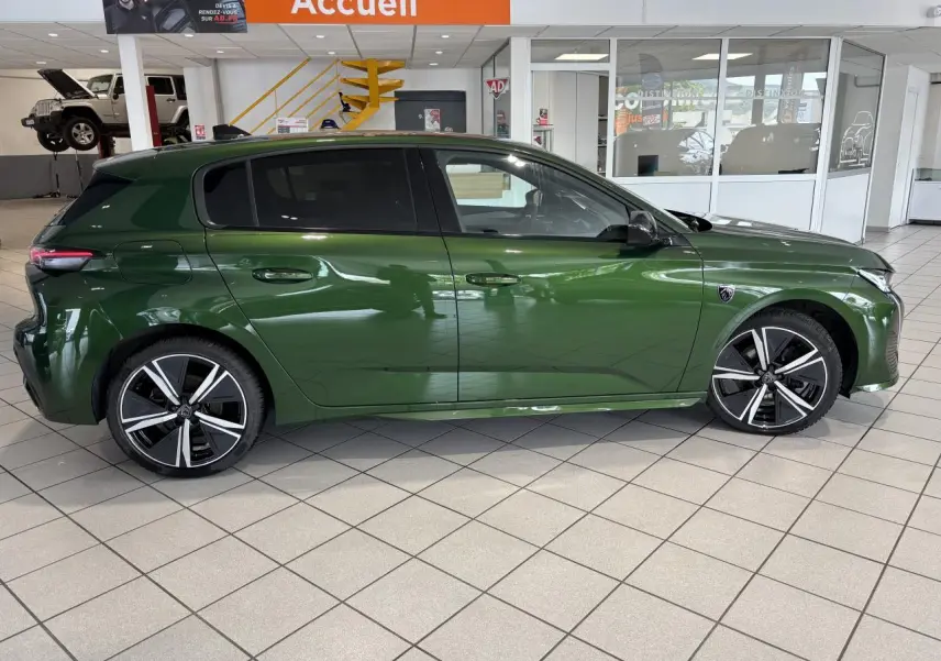 Profil droit de la Peugeot 308 GT 2024 vert métallisé avec jantes alliage 18'' et vitres surteintées en showroom.