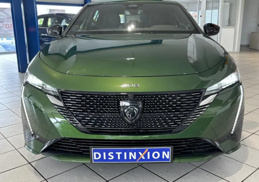 Vue frontale d'une Peugeot 308 berline GT 2024 vert métallisé avec calandre noire et feux LED griffés.