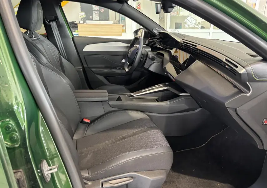 Vue intérieure côté conducteur d'une Peugeot 308 2024 verte, avec sellerie tissu/TEP noire et planche de bord moderne.